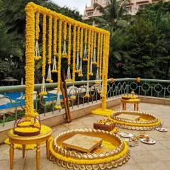 A beautiful poolside Haldi ceremony setup. The decor features a frame draped with yellow marigold garlands and traditional brass urlis for the ceremony, combining tradition with a resort-like feel.
