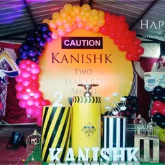 A creative construction theme for a second birthday party. The setup includes a bold "CAUTION" sign on a yellow backdrop, balloon arches in red, yellow, and black, and custom props like themed barrels and vehicle cutouts.