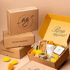 A beautifully arranged Diwali hamper, ready for gifting. This box is filled with festive treats, including a tea cake, cookies in a jar, an AG mug, and decorated with marigold flowers.