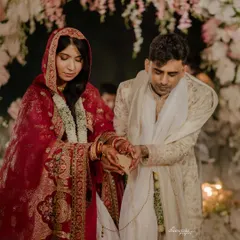 A groom and bride during their wedding ceremony. His sherwani, crafted with over 80 hours of hand embroidery, features soft hues of cream and pink inspired by Koyalia birds, reflecting the venue's tranquil beauty.