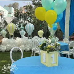 A close-up of the table setting, featuring a centerpiece with a teddy bear and balloons, and a backdrop of hot air balloon props nestled in 'clouds' of white balloons.