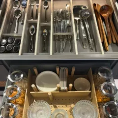 A perfect example of customized drawer organization. The top section uses dividers for cutlery, while the bottom uses adjustable pegs to secure bowls, plates, and jars, preventing them from shifting.