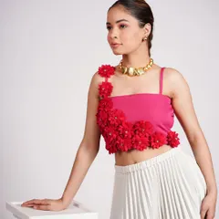 Here, a model wears a pink crop top with red floral details, paired with a white pleated skirt. The gold statement necklace adds a touch of elegance to the modern silhouette.