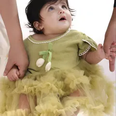 A close-up of a beautiful baby girl in a lovely green dress, securely held by her parents' hands. This shot highlights the delicate details and innocence of infancy.