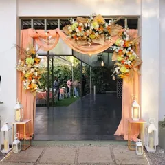 The entrance to this engagement party sets a warm and welcoming tone. A beautiful floral arch in peach and orange hues, complemented by soft drapery and lanterns, invites guests into the celebration.