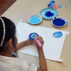 A girl carefully dabs paint onto her bubble wrap stamp. This activity requires focus and helps develop her fine motor skills.