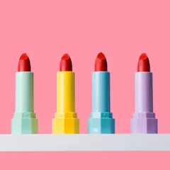A row of colorful lipsticks against a solid pink background. This simple, vibrant, and playful composition is perfect for social media and beauty blogs.