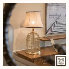 This unique table lamp features a golden birdcage base, offering a touch of whimsy and sophistication. It's a perfect conversation piece for a console table or side table, providing warm light through its classic fabric shade.