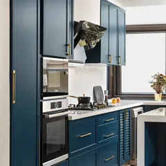 A closer look at the functional side of the blue kitchen. We integrated the oven and microwave into a tall unit for a seamless look and ergonomic use. The slim brass handles add a touch of elegance to the shaker-style cabinets.