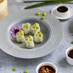A set of delicate edamame dumplings styled with their core ingredient. The clean, bright lighting and minimalist plating on a textured grey plate make this image feel fresh, healthy, and upscale.