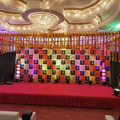 A vibrant and traditional Sangeet stage in a banquet hall. The backdrop features a colorful checkerboard pattern with marigold details, creating a perfect setting for musical performances.