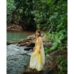 A beautiful outdoor portrait taken during a Haldi photoshoot. The bride to be stands by a flowing stream, with the lush greenery of the Karavali coast creating a stunning natural backdrop.