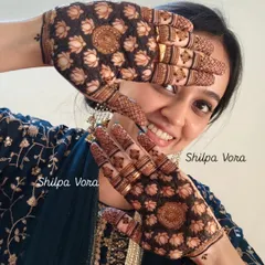A happy client peeking through her hands, adorned with a dense and beautiful lotus 'jaal' design.