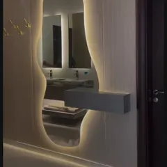 Another modern dressing mirror design. This one features a sleek, asymmetrical shape with integrated backlighting and a small floating shelf, perfect for a contemporary bathroom or dressing area.