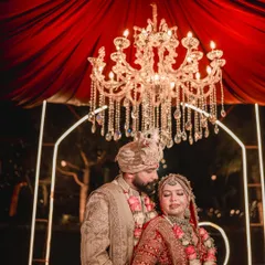 An intimate shot of the couple during their Jaimala ceremony, framed by a magnificent crystal chandelier that adds to the grandeur of the moment.