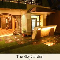 A modern terrace garden featuring a sleek, angular outdoor bar with integrated lighting. The space is defined by a unique flooring pattern of artificial grass and stone, and a circular artistic entryway that adds a sculptural element to the design.
