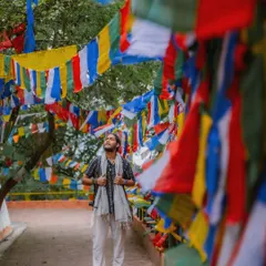 Standing amidst a sea of colorful Tibetan prayer flags in Darjeeling. The composition uses the flags to frame the shot, creating a vibrant image that speaks of peace and spirituality.