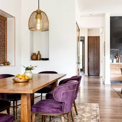 An open-concept dining area where bold purple chairs are paired with a warm wood table and floors. The design feels modern, welcoming, and full of personality.