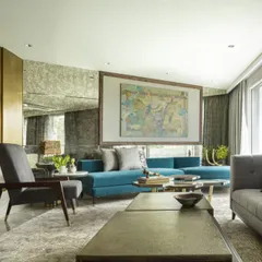 A wide view of the Jor Bagh Residence living room, showcasing a balance between modern aesthetics and comfort. A large traditional painting is given a contemporary frame, and a brass-paneled wall adds a touch of glamour.