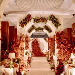 A dramatic and romantic reception entrance, with a long aisle flanked by modern white arches and explosive arrangements of red foliage, leading to a stunning focal point.