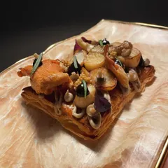 A creative mushroom tartine on a flaky pâte feuilletée base. It's topped with black garlic ketchup, mushroom mascarpone, and a variety of wild mushrooms.
