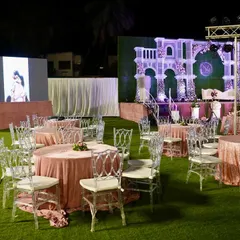 An overview of an outdoor reception setup, showing how we integrate large LED screens and grand stage designs. The blush pink table linens and clear Chiavari chairs add a touch of modern elegance to the space.