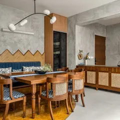 This dining area showcases several custom pieces, from the bench seating with its geometric wood-paneled backdrop to the cane-fronted sideboard. The color palette of turmeric yellow and grey adds a unique vibrancy.