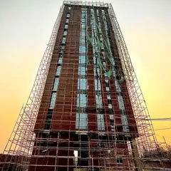 A frontal shot of the same tower under construction. This image provides a clearer view of the exposed brickwork and window placements, showing the raw structure before final completion.