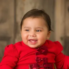 A close-up of the birthday girl's happy face. Her sweet smile and the festive red bows on her dress make this a perfect first birthday portrait.
