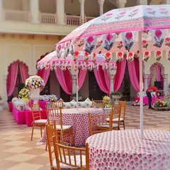 A daytime Mehendi function held in a palace courtyard, featuring decor inspired by Rajasthani block prints. The custom-printed umbrellas and tablecloths, paired with bright pink drapes, created a festive and culturally rich setting.