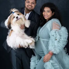 A smiling couple poses for a maternity portrait with their fluffy Shih Tzu, showcasing our pet-friendly studio environment.