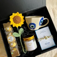 The 'Jigar Ka Tukda' hamper for your sister, themed around the protective evil eye. It features an evil eye mug, a matching rakhi, a crochet sunflower, and her favorite chocolates.