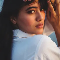 An over-the-shoulder pose captured at the beach during sunset. The warm light kisses the model's cheek and hair, creating a beautiful, soft glow. This kind of shot feels intimate and candid, perfect for a natural beauty campaign.