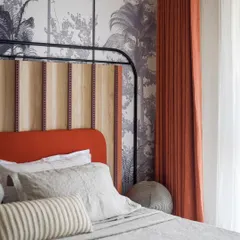 A detail shot of the custom tropical wallpaper and upholstered headboard in the master bedroom. The vibrant orange and natural wood tones bring a touch of the tropics indoors.