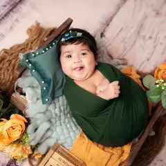 This happy baby girl, wrapped in a dark green swaddle, gives the camera a big, tongue-out smile.