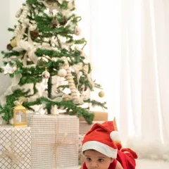 Celebrate your baby's first Christmas with a festive photoshoot. This setup includes a decorated tree, presents, and a cute Santa hat for a perfect holiday card photo.
