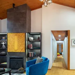 A closer look at the living area, where a bold blue Ava chair adds a pop of color against the warm wood and ash-grey fireplace. The space is a journey of details, from the curated books on the shelves to the art that hangs above the hearth.