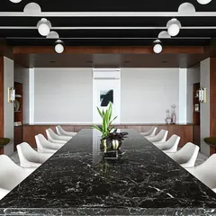 This executive conference room features a massive, single-slab black marble table as its centerpiece. The dark wood paneling, integrated bench seating, and dramatic ceiling lights create a formal yet inviting atmosphere for important meetings.