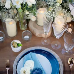 A beautiful and modern tablescape with blue and white plates, custom acrylic name cards, and a centerpiece of white flowers and candles.