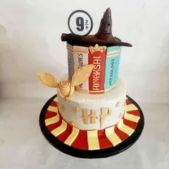 A magical two-tier Harry Potter cake, perfect for any fan. This design features the sorting hat, a golden snitch, and edible books, with a Gryffindor-striped bottom tier to complete the Hogwarts theme.
