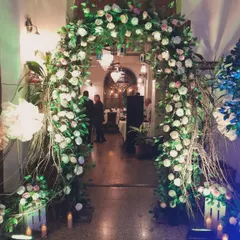 A grand entrance arch made with an abundance of white and pink roses and rustic branches. This type of floral entrance decoration sets a luxurious and welcoming tone for any high-profile corporate event.