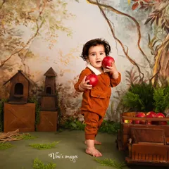 An apple a day. This toddler portrait captures a moment of discovery as the child holds up two bright red apples in our charming, hand-painted forest backdrop.