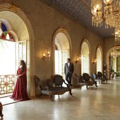 A couple stands framed in an ornate archway of a palace hall, with grand chandeliers and marble floors creating a sense of timeless elegance. This pre-wedding shoot in Hampi showcases how I use architectural elements to create stunning, regal portraits.