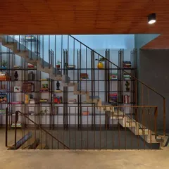 This statement staircase is a functional sculpture, with its concrete steps appearing to float against a backdrop of a floor-to-ceiling bookshelf made of slender metal rods. It's a design that integrates storage and circulation into a single, striking feature.