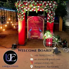 A personalized welcome board for an outdoor wedding, framed by a red floral arch. This setup not only greets guests but also serves as a beautiful photo opportunity at the entrance of the venue.