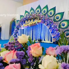 A beautiful angle of the Krishna theme backdrop, seen through a foreground of fresh pink and purple flowers, adding depth and color to the scene.