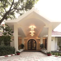 A closer view of the Doon Homestay's entrance portico. The design balances architectural form with soft landscaping, using potted plants and low hedges to soften the lines and guide visitors toward the arched doorway.