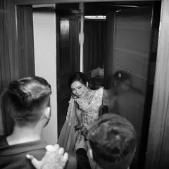 A candid moment captured in monochrome. The bride peeks out from a doorway with a joyful laugh, and the black and white treatment emphasizes the raw emotion and happiness of the moment.