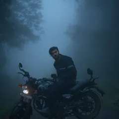 A rider sits on a Royal Enfield Hunter 350, enveloped in dense, blue-toned fog on a remote road. This moody motorcycle portrait captures the quiet solitude and atmosphere of a monsoon ride through the ghats.