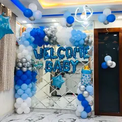 Welcoming a new baby is a special occasion, and we decorate your home to make it perfect. This is a 'Welcome Baby' boy setup with a blue and silver balloon arch against a modern mirror wall, creating a clean and celebratory look.
